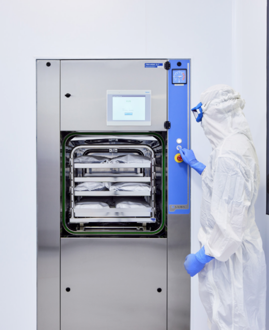 A worker in a white clean suit pressing a button on a steel machine